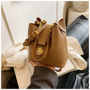 Détail montrant la boucle dorée brillante et le pendentif pièce sur un sac seau marron