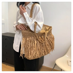 Dettaglio della borsa tote in paglia boho con lunghe frange e doppi manici con outfit casual
