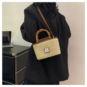 Detail of a woven straw crossbody bag featuring bamboo handles and brown leather strap