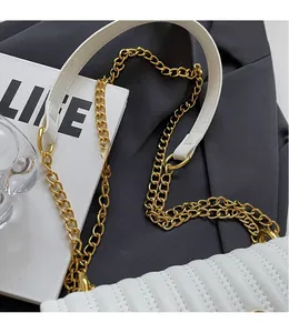 Detail view of quilted white PU leather shoulder bag with a gold chain strap on grey fabric