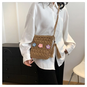 Detail of woven straw crossbody bag featuring colorful crochet flowers and fringe tassel