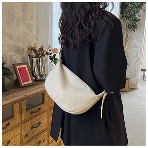 Minimalist cream semi-circle crossbody bag with pebbled texture on a stylish model
