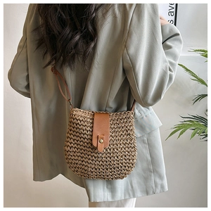 Close-up of woven straw crossbody bag with brown leather strap and buckle detail