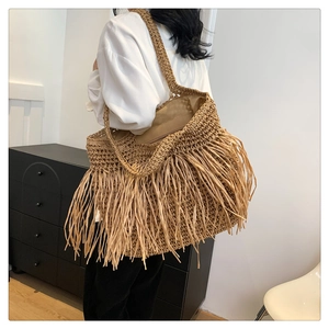 Dettaglio di una borsa tote in paglia intrecciata con lunghe frange boho e doppie tracolle