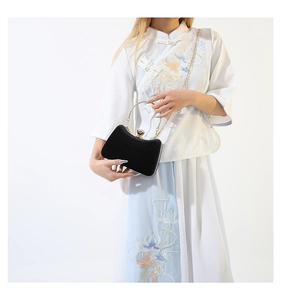 Close-up of black velvet evening clutch with gold metal handle and rhinestone clasp detail
