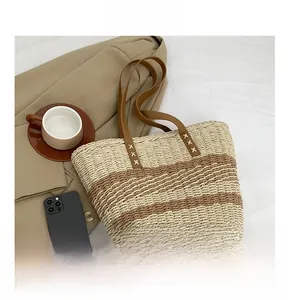 Close-up of woven straw tote bag featuring contrast stitching and faux leather handles