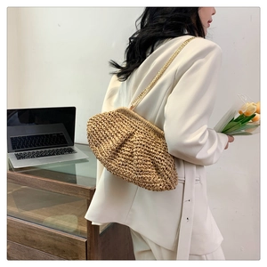 Detail of a natural woven straw clutch bag with golden chain strap on a white blazer