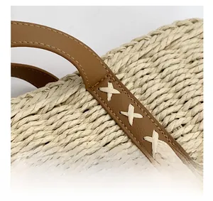 Close-up of woven straw handbag showing brown leather handle with white cross-stitching details