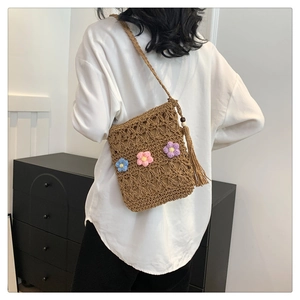 Close-up of woven straw crossbody bag with floral ornaments and long decorative tassels