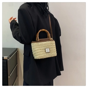 Detail of woven straw bag with bamboo handle and leather trim worn with black blazer