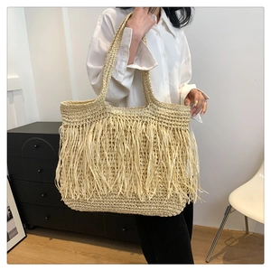 Dettaglio di una borsa tote in paglia beige con nappe decorative e ampia tracolla comoda
