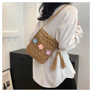 Detail view of woven straw shoulder bag featuring colorful crochet flowers and long tassel