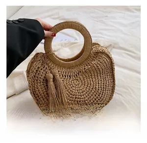 Detail view of woven khaki handbag with round handle and tassel on white fabric