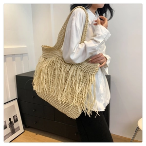 Dettaglio della borsa a tracolla in paglia beige con lunghe nappe e trama intrecciata