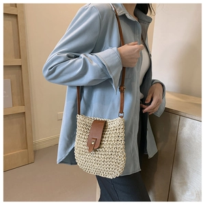 Detailed shot of hand-woven straw crossbody bag with brown leather flap and retro buckle