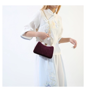 Macro shot of burgundy velvet evening bag with gold metal clasp and elegant chain strap