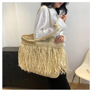 Dettaglio di borsa tote in paglia beige intrecciata con lunghe nappe per look estivo
