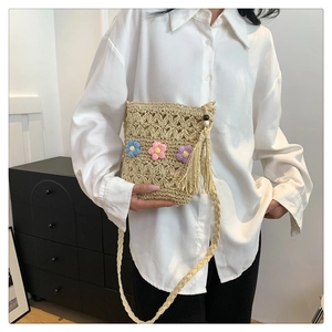 Close-up of beige woven straw shoulder bag with colorful 3D flowers and long tassels