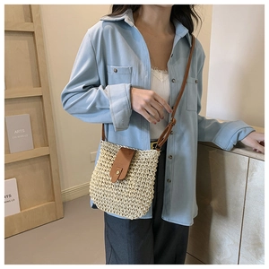 Close-up of woven straw shoulder bag with brown leather flap and vintage metal buckle