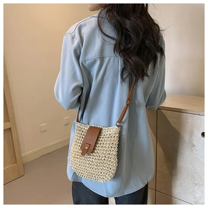 Detail of woven straw crossbody bag with brown faux leather flap and gold buckle detail