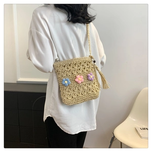 Detail view of khaki straw crossbody bag with colorful crochet flowers on a model