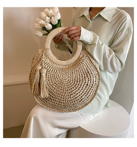 Detail of hand-woven round straw handbag with circular handle and twin tassels decoration