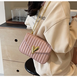 Detail of pink quilted PU leather bag with golden heart buckle and chain strap on a model
