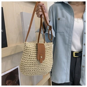 Detail of woven straw crossbody bag featuring brown leather trim and magnetic snap closure