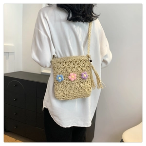 Detail of straw woven crossbody bag featuring colorful knit flowers and wood bead tassel