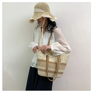 Detail of woven straw tote bag with brown leather handles and striped texture