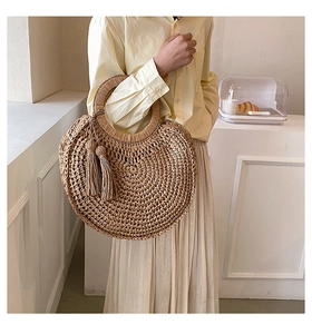 Detail of hand-woven round straw handbag with bohemian tassel charm and top handle