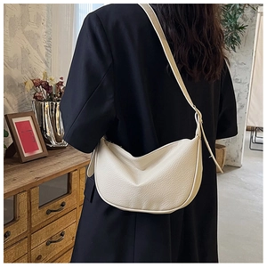 Chic beige crescent bag in pebbled faux leather worn on shoulder in a retro setting