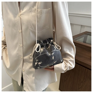 Detail of grey fabric bucket bag featuring pink floral embroidery and woven strap