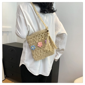 Detail of woven straw crossbody bag with colorful crochet flowers and long side tassels