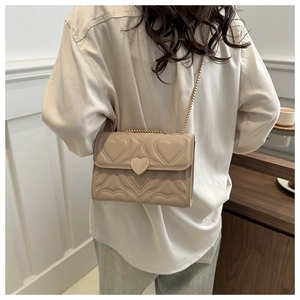 Detailed view of beige heart-quilted crossbody bag with gold chain strap and heart buckle