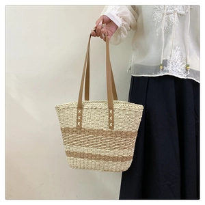 Detail of hand-woven striped straw tote bag with premium brown leather handles and stitching