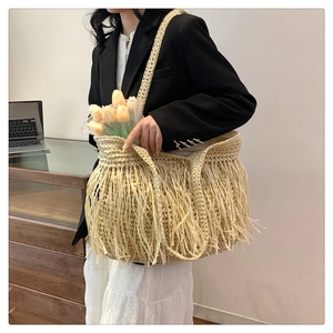 Dettaglio ravvicinato della borsa tote in paglia con frange decorative e tracolla larga