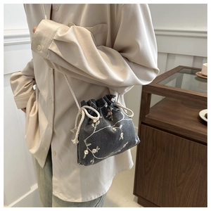 Detail of grey crossbody bucket bag with floral embroidery and white rope strap
