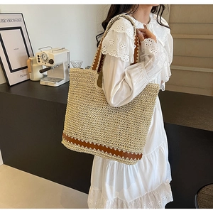 Close-up of woven straw tote bag with brown leather trim held by a model in casual style
