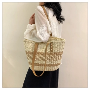 Close-up of woven straw tote bag featuring brown leather handles and striped texture