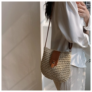 Detailed view of a woven straw shoulder bag with brown leather flap and bronze rivets