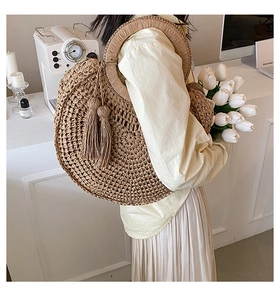 Close-up of a stylish round straw handbag with elegant tassels in a minimalist setting