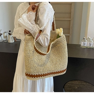 Detail of woven straw tote bag with brown scalloped leather trim and shoulder strap