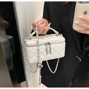 Macro detail of white quilted mini bag showing gold ball chain and dual zippers