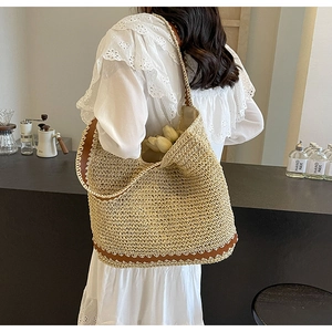 Straw woven tote bag with brown leather trim carried by model in a rustic cafe setting