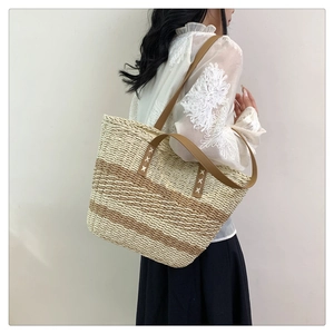 Detail view of woven striped tote bag with brown leather handles and cross-stitch detail