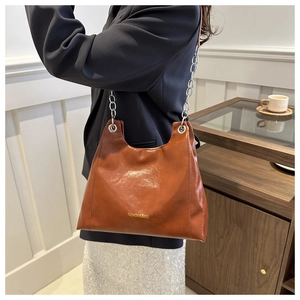 Dettaglio di una borsa a spalla in pelle marrone con una grande catena in metallo