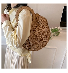 Fashionable round straw handbag with ring handle and tassel shown on a stylish model