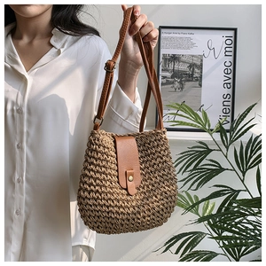 Detailed view of woven straw shoulder bag with brown leather flap and gold metal clasp