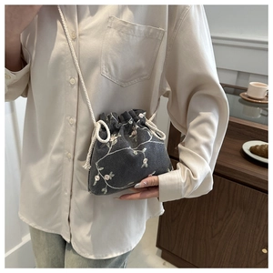 Detail of grey fabric bucket bag with floral embroidery and white braided shoulder strap